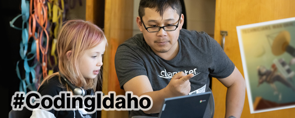Instructor pointing at a student's laptop with the text "#CodingIdaho" in the bottom left corner